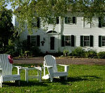 Two white Adirondack chairs in the grass with Captain's House Inn in the background