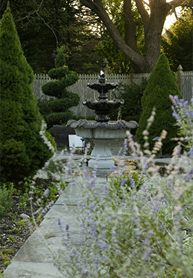 Trickling fountain in herb garden showing trimmed shrubbery and lilac flowers
