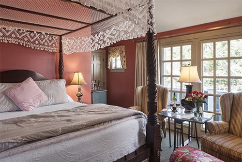 Cape Lady guest room with large window, four poster canopy bed with lace canopy and wingback chairs