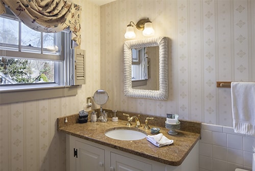 Cape Lady guest bath with papered walls, window, vanity, mirror and sconce light