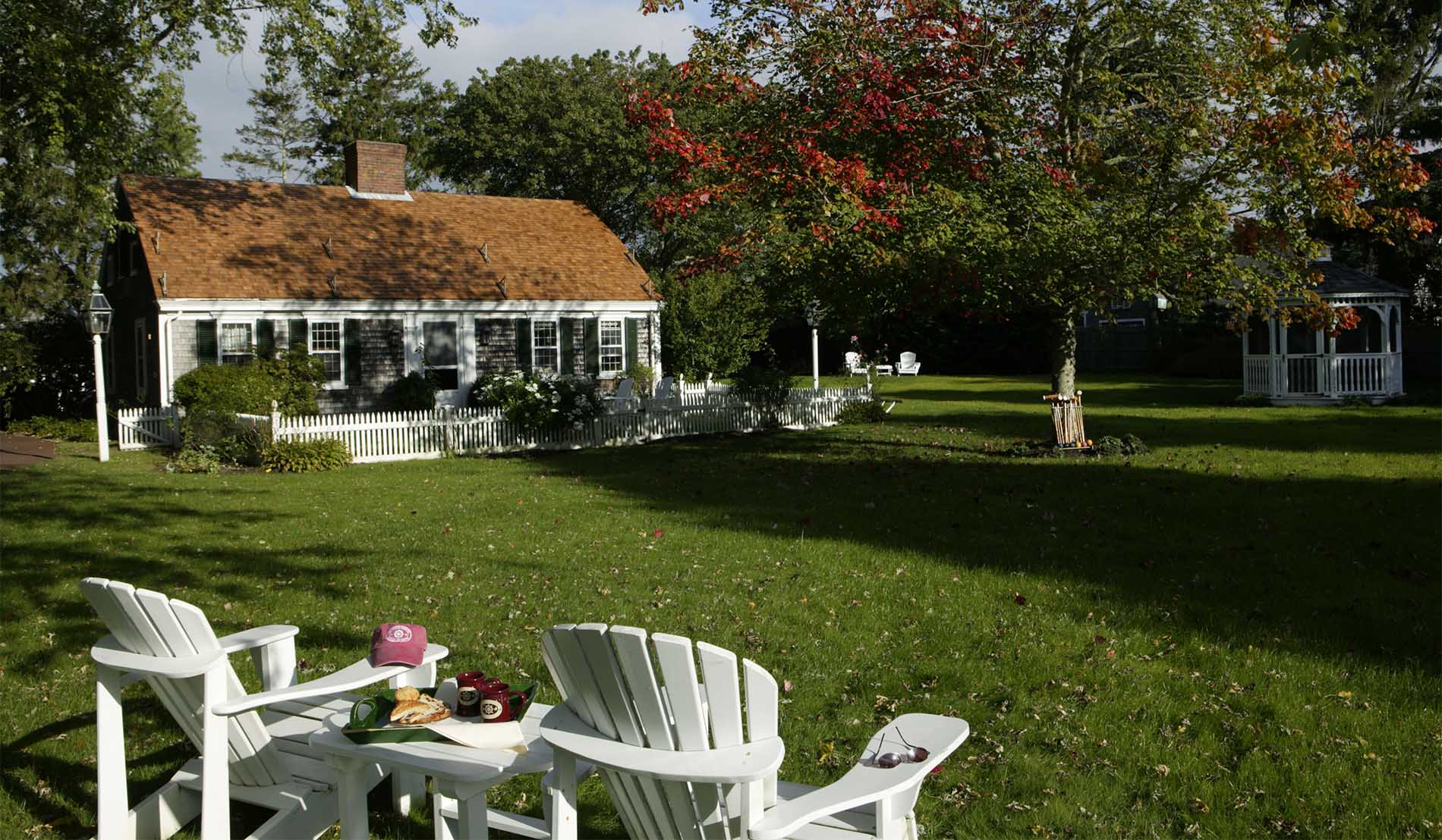 Exterior view of Captains Cottage with white Adirondack chairs and gazebo