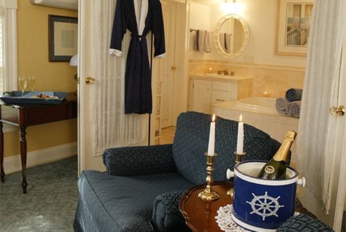 Clarissa guest room with upholstered sitting chair, chilled Champagne and view of private bath with navy robe