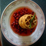 White plate trimmed in pale flowers topped with a stack of small waffles surrounded by berries