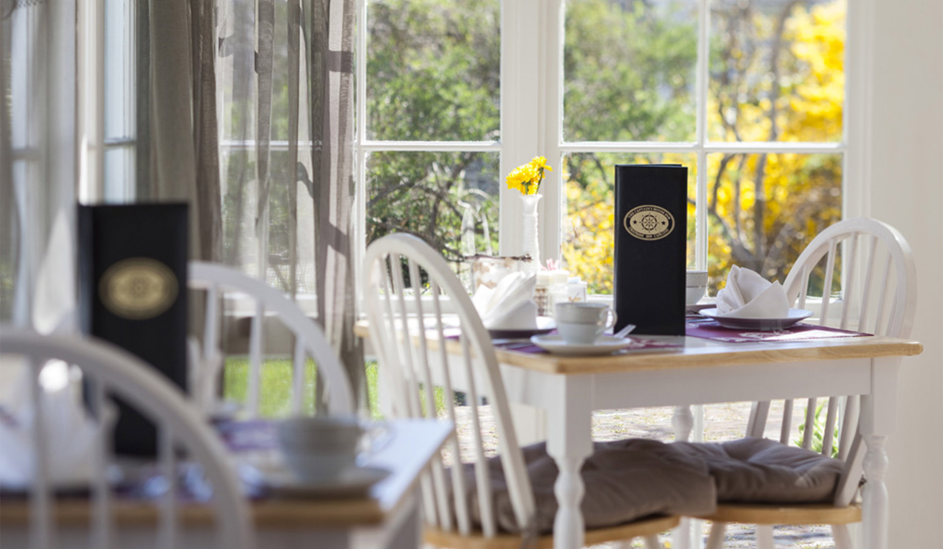 Table in the dining room showing setting for two and bud vase with yellow flowers