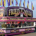 Large fried dough stand at a carnival selling funnel cakes, drinks and fried dough