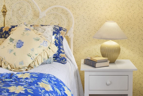 Garden guest room with white bed, blue and yellow bedding and white nightstand with yellow papered walls