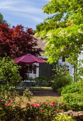 Red patio umbrella and metal chairs nestled in the beautiful gardens at the Inn