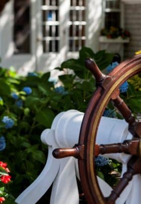 Captain's wheel yard ornament with blue hydrangea and red flowers