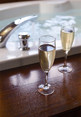 Two Champagne flutes next to a soaking tub full of water