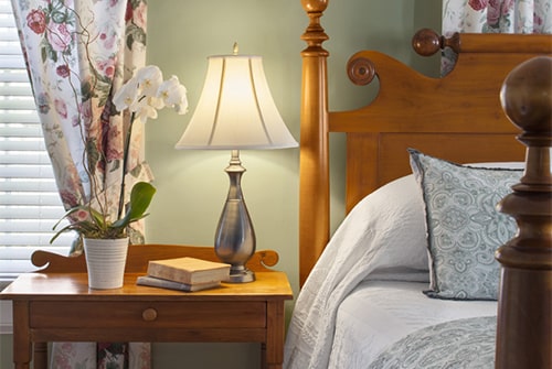 Hannah Rebekah guest room with wood bed and nightstand, windows with floral curtains