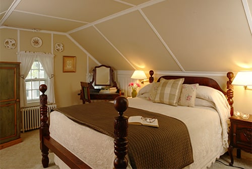 Hideaway Suite showing bedroom with queen bed and beige bedding, vanity area, and window with white curtains