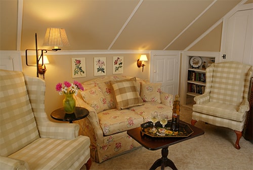Hideaway Suite with pale yellow loveseat, wingback chairs, table with snacks and sconce lighting