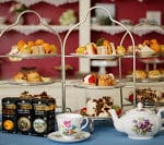 Three three-tiered dessert stands filled with snacks and a teapot with cups and saucers