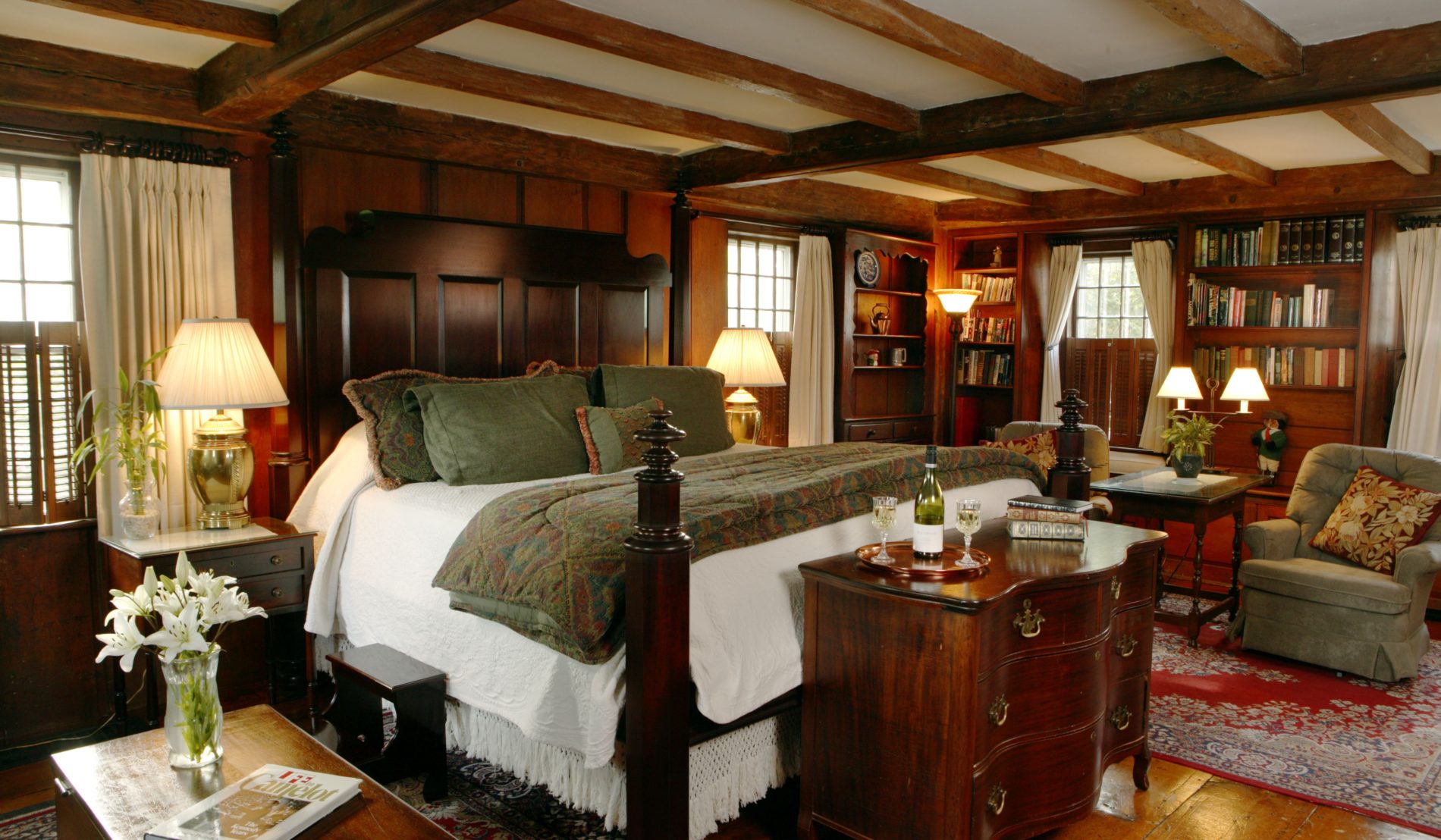Hiram Harding cottage with ceiling beams, wide plank wood floor, four poster bed, several windows, cozy sitting chairs and bookshelves