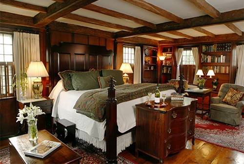 Hiram Harding guest room showing carved king bed with burgundy, gold, and deep green bedding and pumpkin wood paneled walls