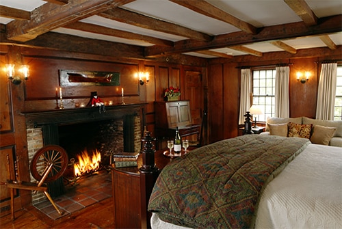 Hiram Harding Guest Room with paneled walls, fireplace, windows and quilted bed