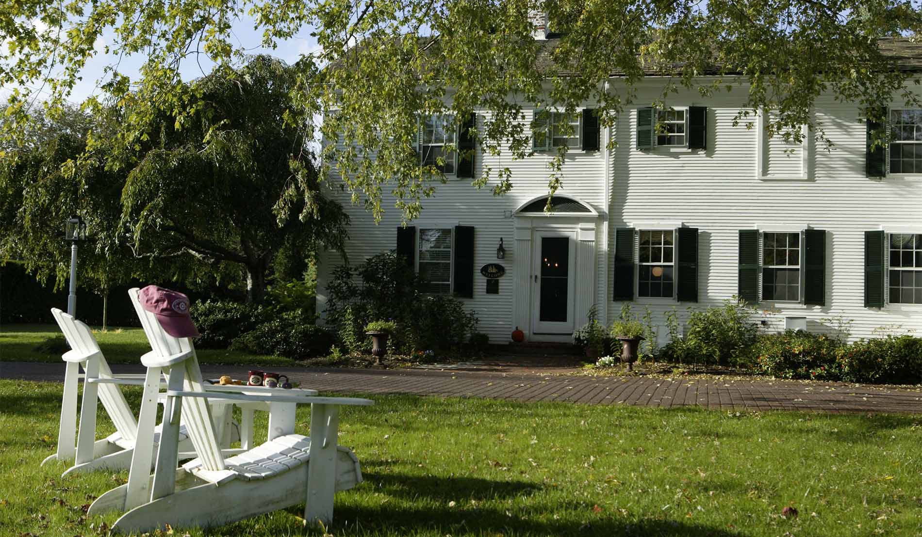 Two white Adirondack chairs sitting in the grassy lawn in front of the two-story white sided Inn