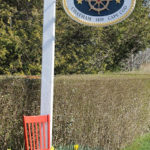 Red wooden chair sitting in grass next to yellow flowers and tall white sign: Captain's House Inn, Chatham 1839 Cape Cod