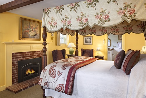 Intrepid guest room showing yellow painted walls, queen bed, and gas fireplace