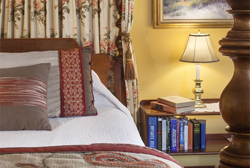 Intredpid guest room with wood bed, brown and red bedding, nightstand with lamp and books