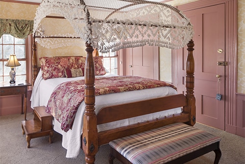 Lady Hope guest room showing queen canopy bed and decorative bench in pinks, yellows, and greens