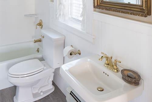 Lady Hope guest bath with tub, small window and white pedestal sink with gold mirror