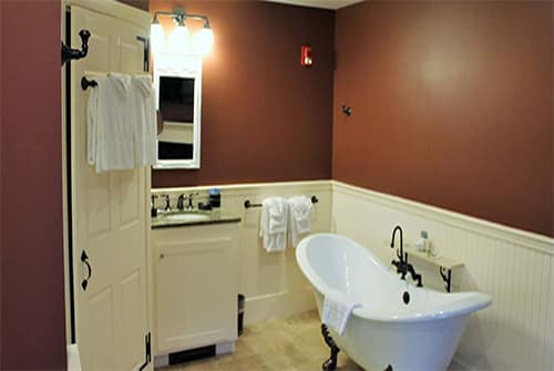 Lady Mariah bathroom showing deep red painted walls, marble vanity sink, and claw foot double soaking tub