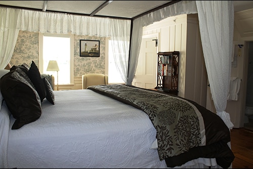 Lady Mariah guest room showing king bed with white bedding and gathered canopy draping and wingback reading chairs in background