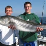 Two young men on a boat holding a huge fish