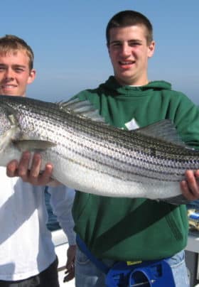 Two young men on a boat holding a huge fish