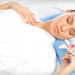 Woman in white robe and towel on her head lying on a massage table holding a flower