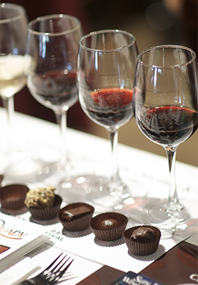 Row of wine glasses with red wine and pieces of chocolate