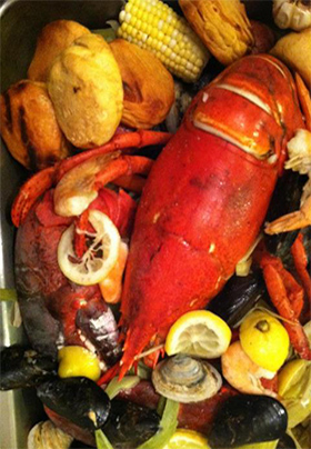 Close-up view of a fish boil with lobster, lemon slices, corn, potatoes