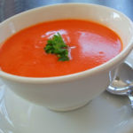 White saucer and bowl filled with orange soup and sprig of greenery