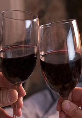 Two people holding wine glasses filled with red wine