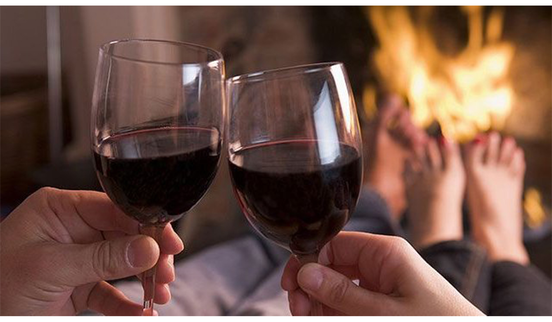 Couple in front of fireplace toasting with red wine in glasses