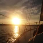 View from a sailboat of the sun about to set over the water