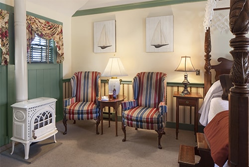 Tradewinds guest room showing striped wingback reading chairs and white enamal potbelly stove gas fireplace.