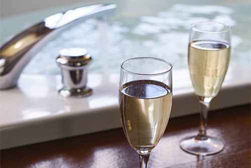 Two wine glasses on the edge of a soaking tub filled with water