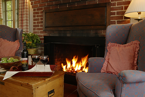 Whirlwind guest room showing red quilted bedding, gas fireplace, and two wingback reading chairs