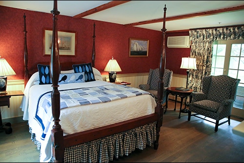 Wild Hunter guest room showing queen four poster bed with blue quilted bedding, red wallpaper, and wingback reading chairs