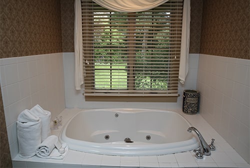 Wild Hunter guest bath with white tiled soaking tub, white towels and window