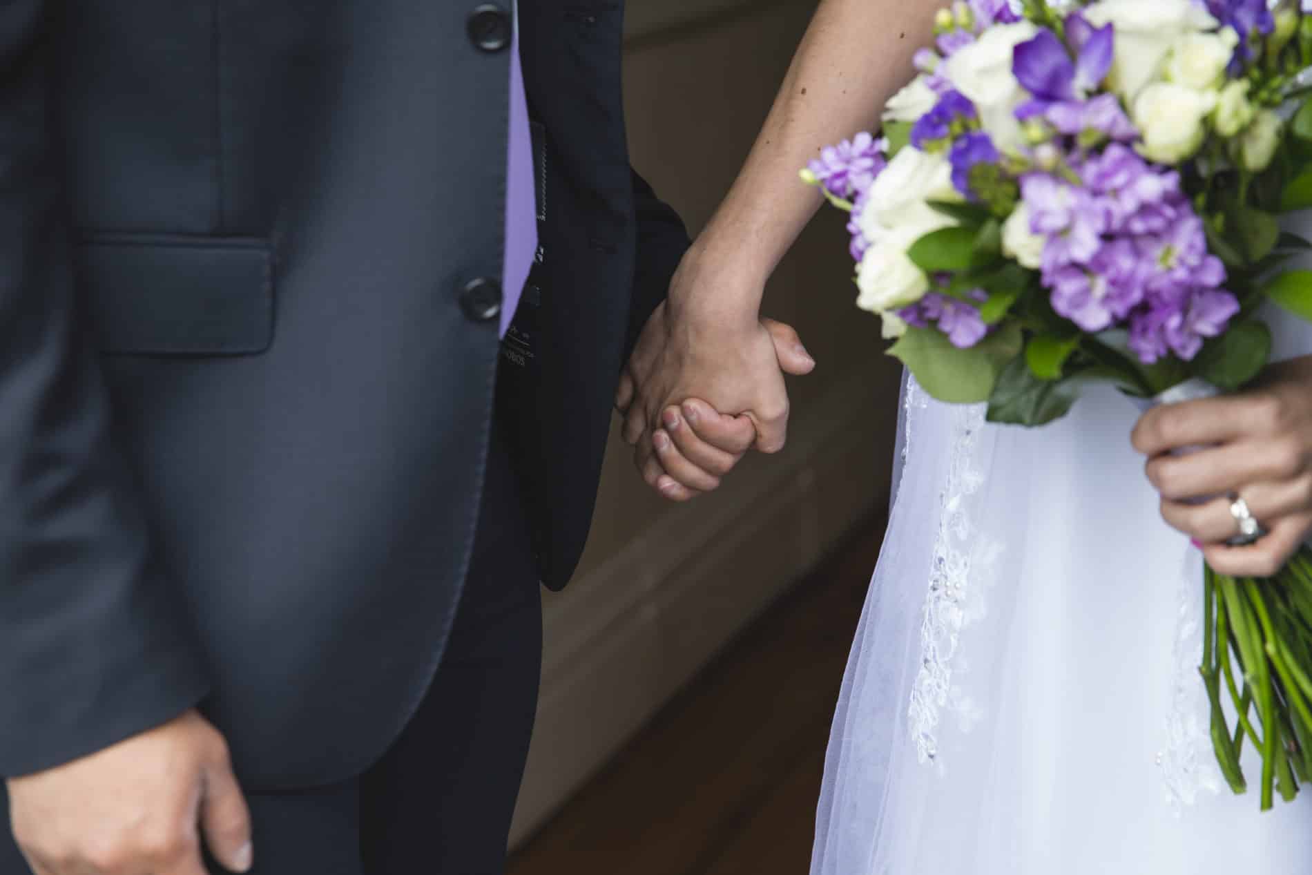 Bride and Groom holding hands with purple and white bridal bouquet