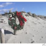 Green wrath with red bow hanging on a wood post on the sandy beach amidst blue skies