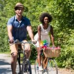 A young couple biking on a paved bike path with surrounding greenery.