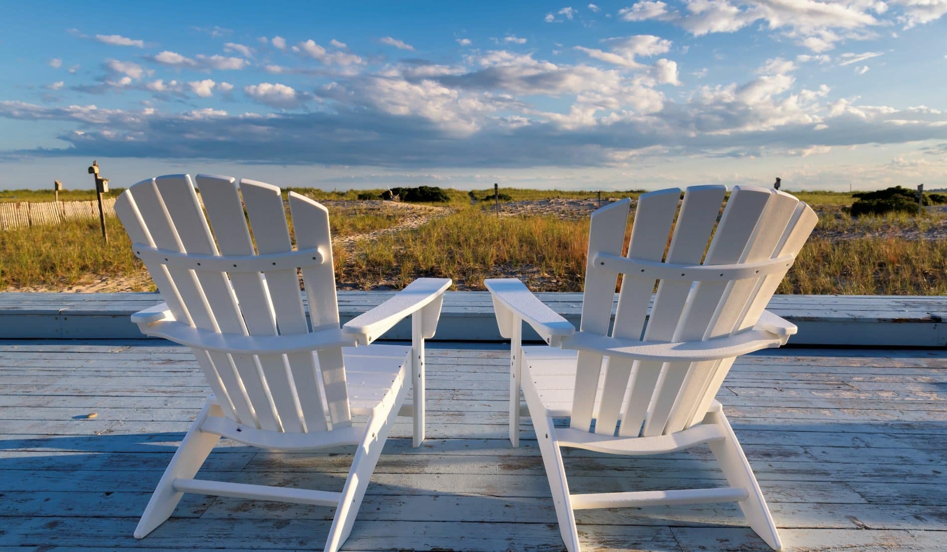 Two white deck chairs looking out at the Cape Cod sand dunes.