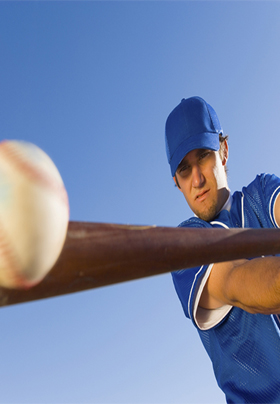 Close-up view of a man in blue with blue cap hitting a baseball with a bat