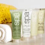 Four small Spa H2O toiletry tubes next to a white towel