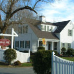 Exterior view of Captain's House Inn with white picket fence, bare trees and blue skies