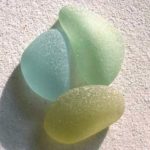Three pieces of smooth sea glass in yellow, blue, and green, sitting in the sand